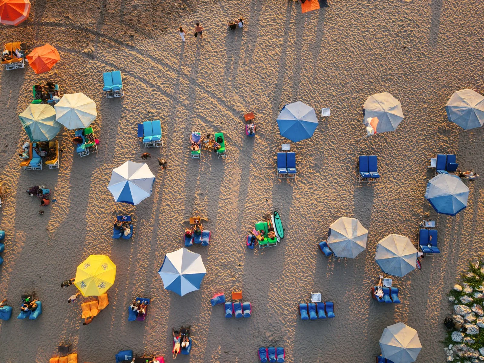 Aerial shot of colorful umbrellas and people relaxing on a sandy Bali beach.