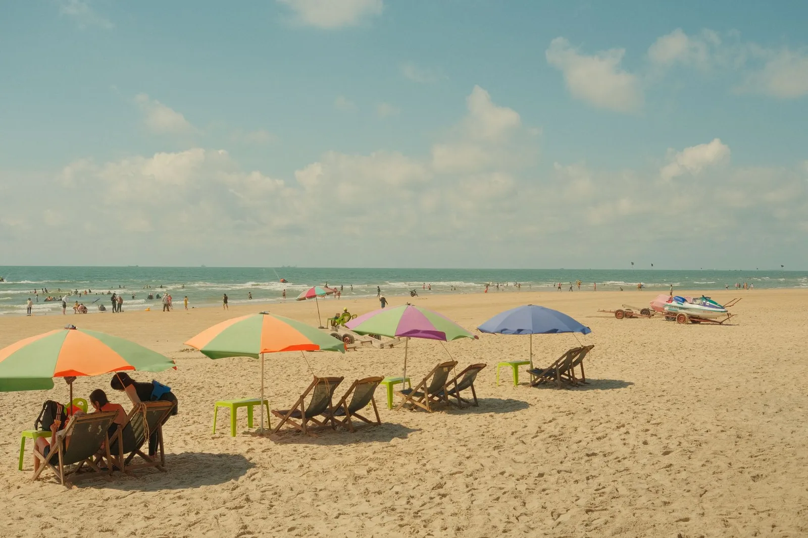 Malerischer Strand mit bunten Schirmen, Stühlen und Menschen, die einen sonnigen Tag genießen.