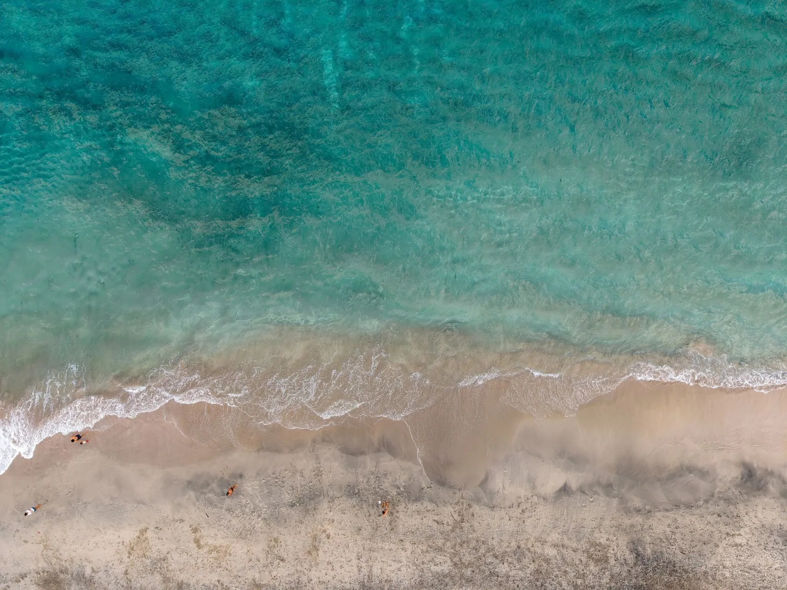 Aerial shot of pristine sandy beach and turquoise ocean in Bali, Indonesia, with people enjoying the scenery.