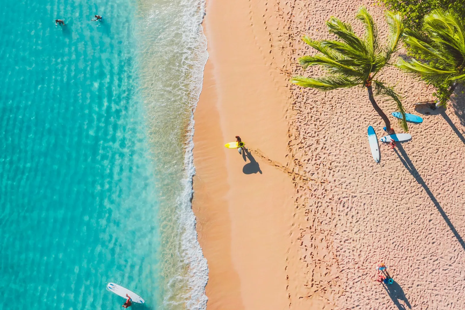 Aerial view of a tropical beach with surfers and turquoise water.