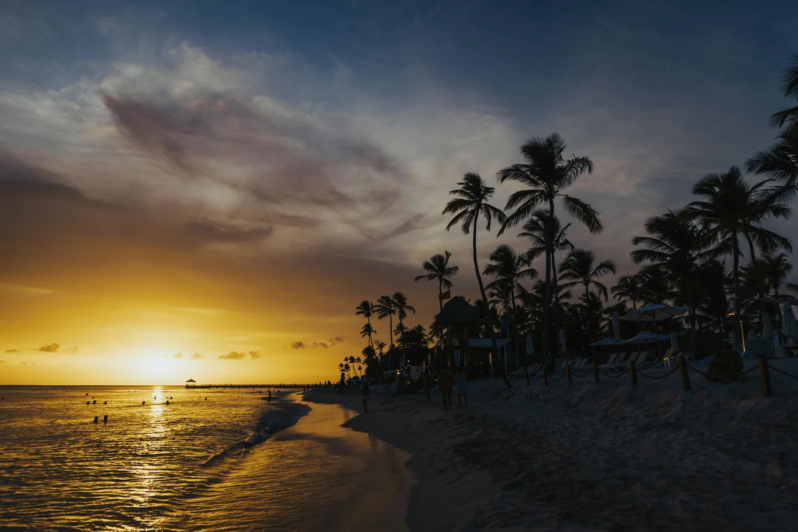 Golden sunset over a tropical beach with palm trees and calm waters, perfect for a tranquil escape.