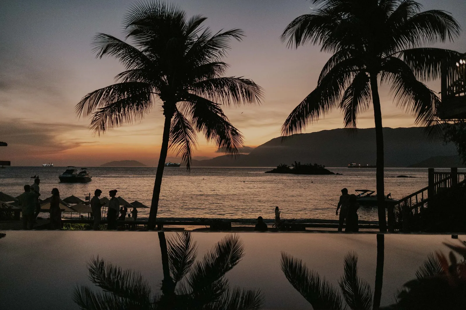 Malerischer Tropensonnenuntergang mit Palmen und Silhouetten am Meer, ideal für Reisemotive.