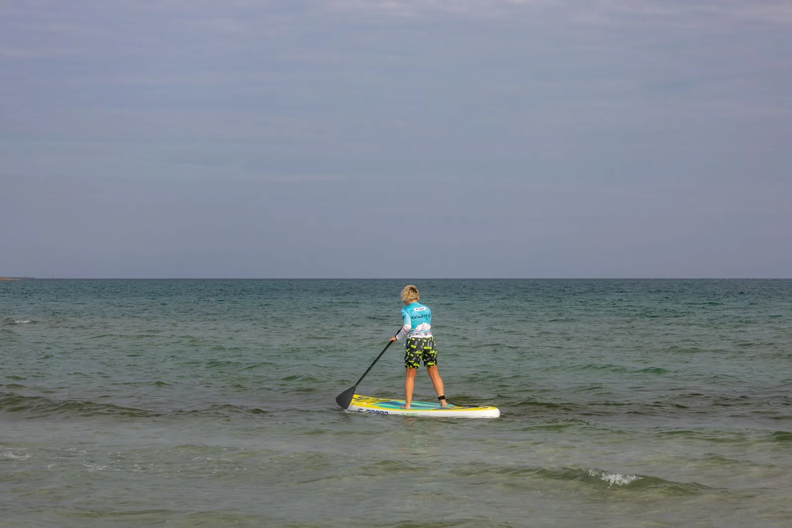 Person paddleboarding on a calm sea under a clear sky, enjoying outdoor recreation.
