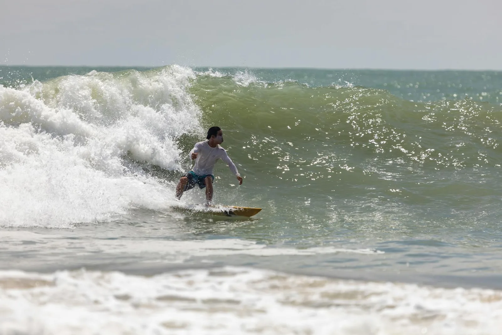 A surfer skillfully navigates a large ocean wave on a sunny day, showcasing surfing expertise.