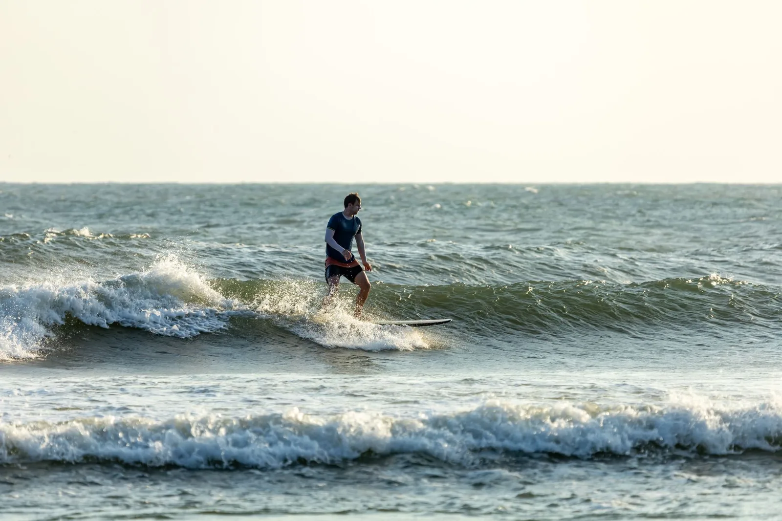 A lone surfer skillfully navigates gentle waves under a warm sunset sky.