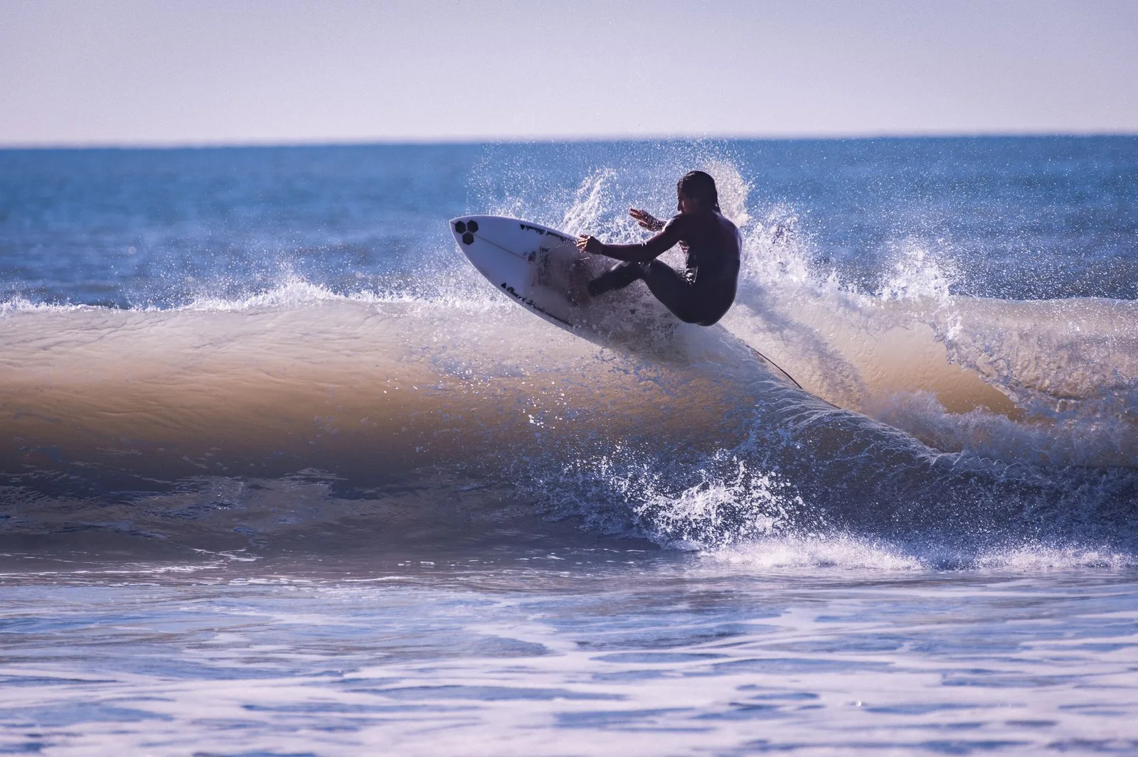 Surfer performing an aerial trick on ocean waves under bright sunlight.